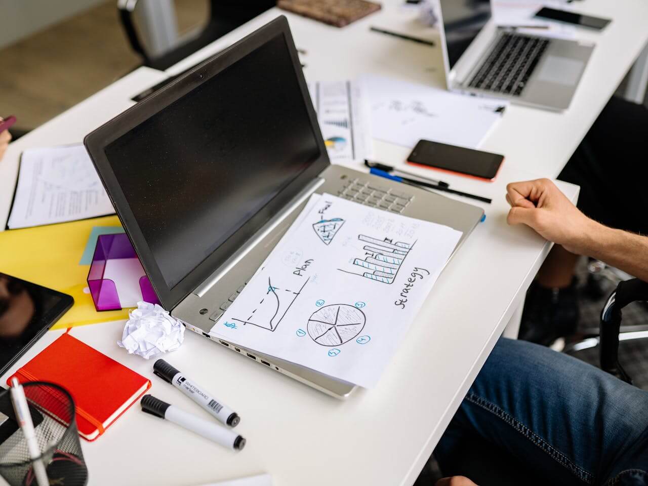 Collaborative workspace with laptops, strategy charts, and planning documents, showcasing the expertise of a leading digital marketing agency in Pakistan.
